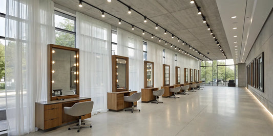 A row of modern salon stations featuring large, LED-lit mirrors and comfortable styling chairs.